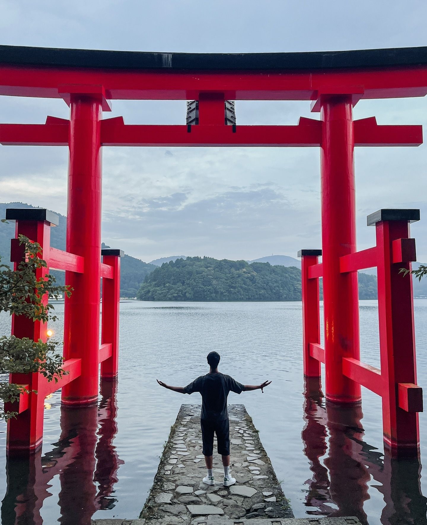 Imaad with arms outstretched in front of a torii gate standing in the water at Hakone Shrine